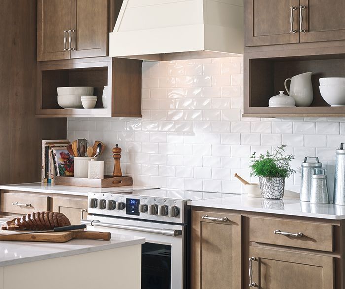 Kitchen with brown cabinets, white countertops, and a stove, with white backsplash and light-colored hood over the stove.