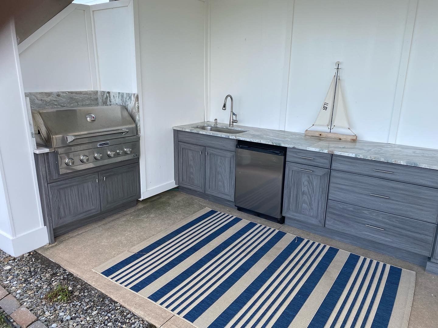 Outdoor kitchen with gray cabinets, stainless steel grill, sink, and striped rug.