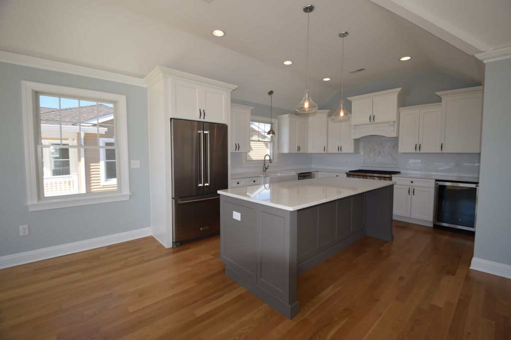 Kitchen with white cabinets, gray island, stainless steel appliances, and hardwood floors.