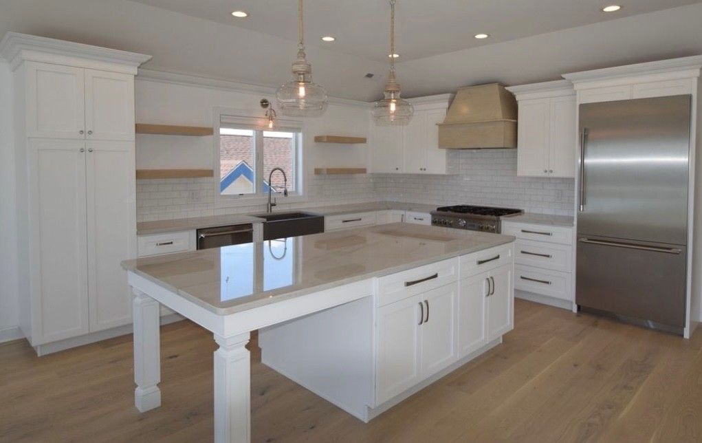 White kitchen with island, stainless steel fridge, and wooden floors.
