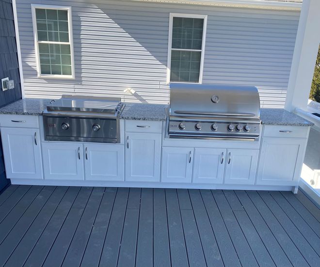 Outdoor kitchen with white cabinets, stainless steel grills, and gray countertops.