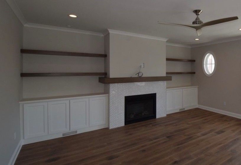 Living room with fireplace, built-in shelves, white cabinets, and wood floors. Neutral tones and recessed lighting.
