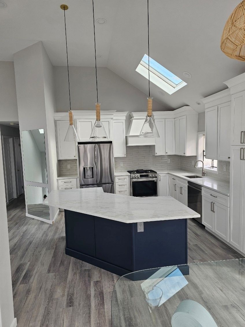 A modern kitchen with a blue island, white cabinets, and pendant lights; gray flooring.