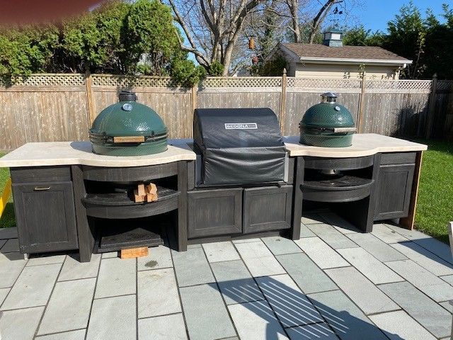 Outdoor kitchen setup with a grill and two Big Green Eggs, on a patio.