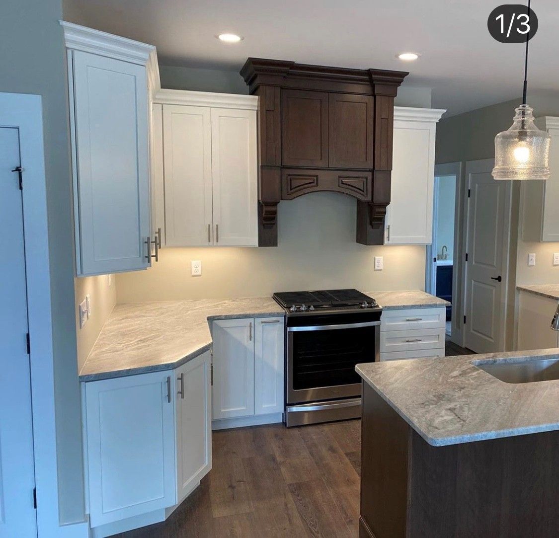 Kitchen with white cabinets, dark hood vent, and stainless steel appliances.