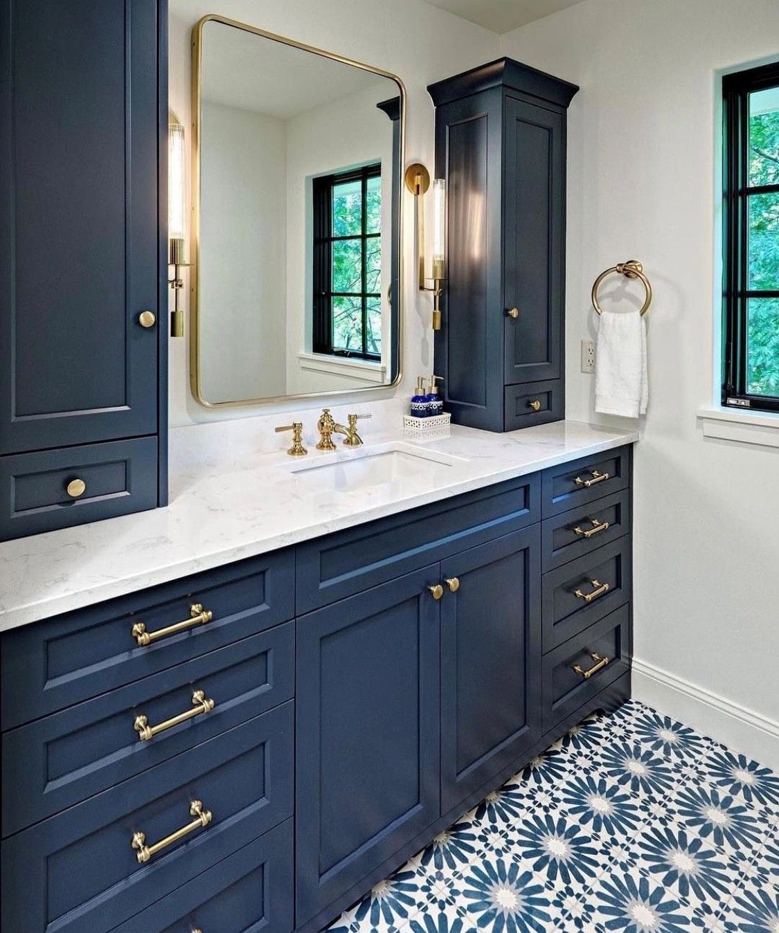 Navy blue bathroom vanity with gold hardware, white countertop, and patterned tile flooring.