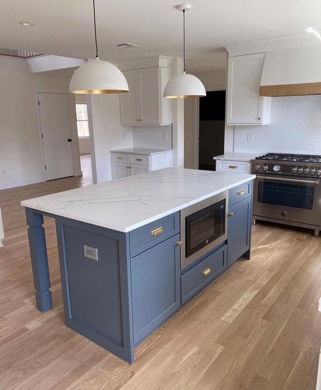 Blue kitchen island with white countertop, built-in microwave, pendant lights, and light wood floors.
