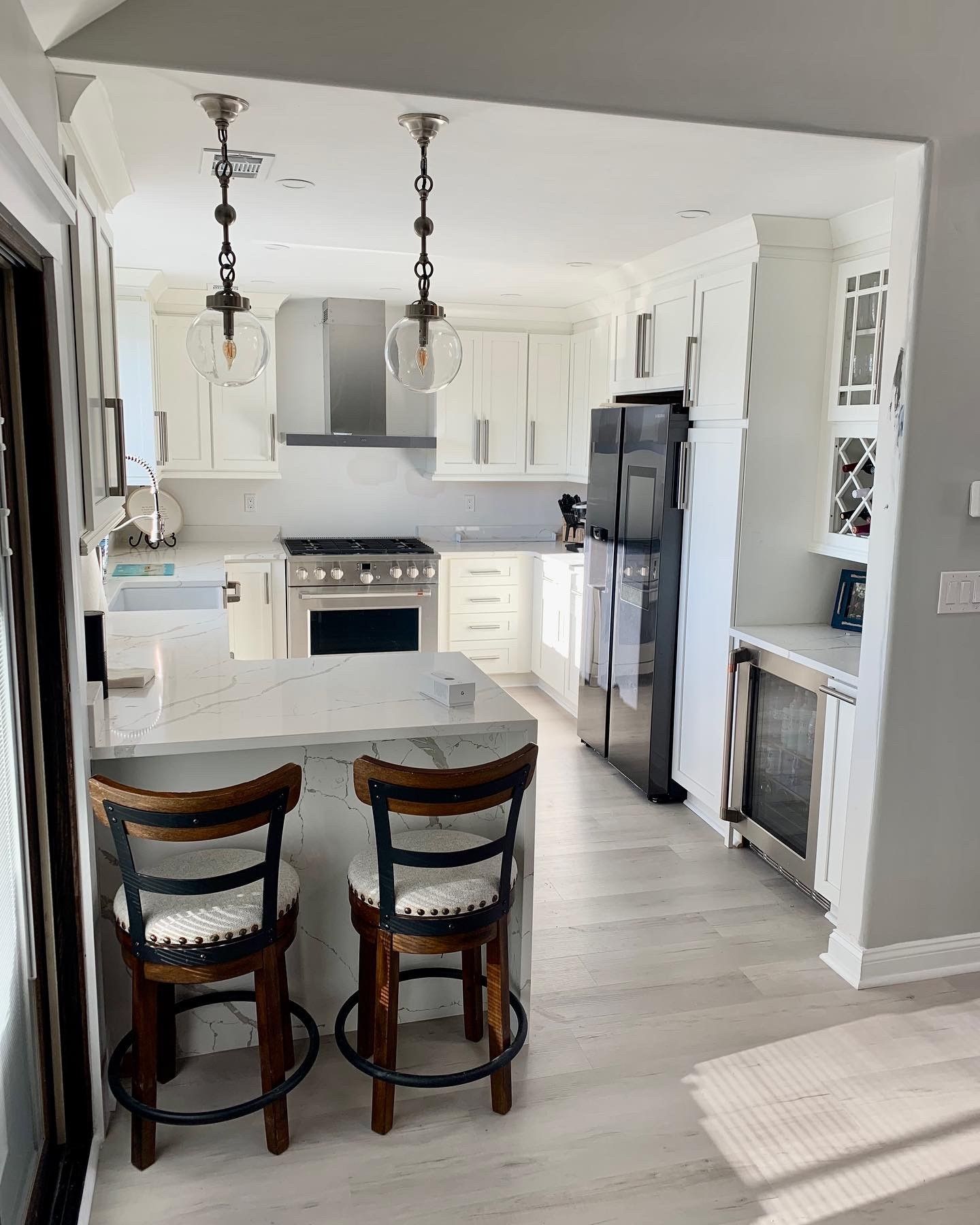 Kitchen with white cabinets, gray countertop, stainless steel appliances, and two bar stools.