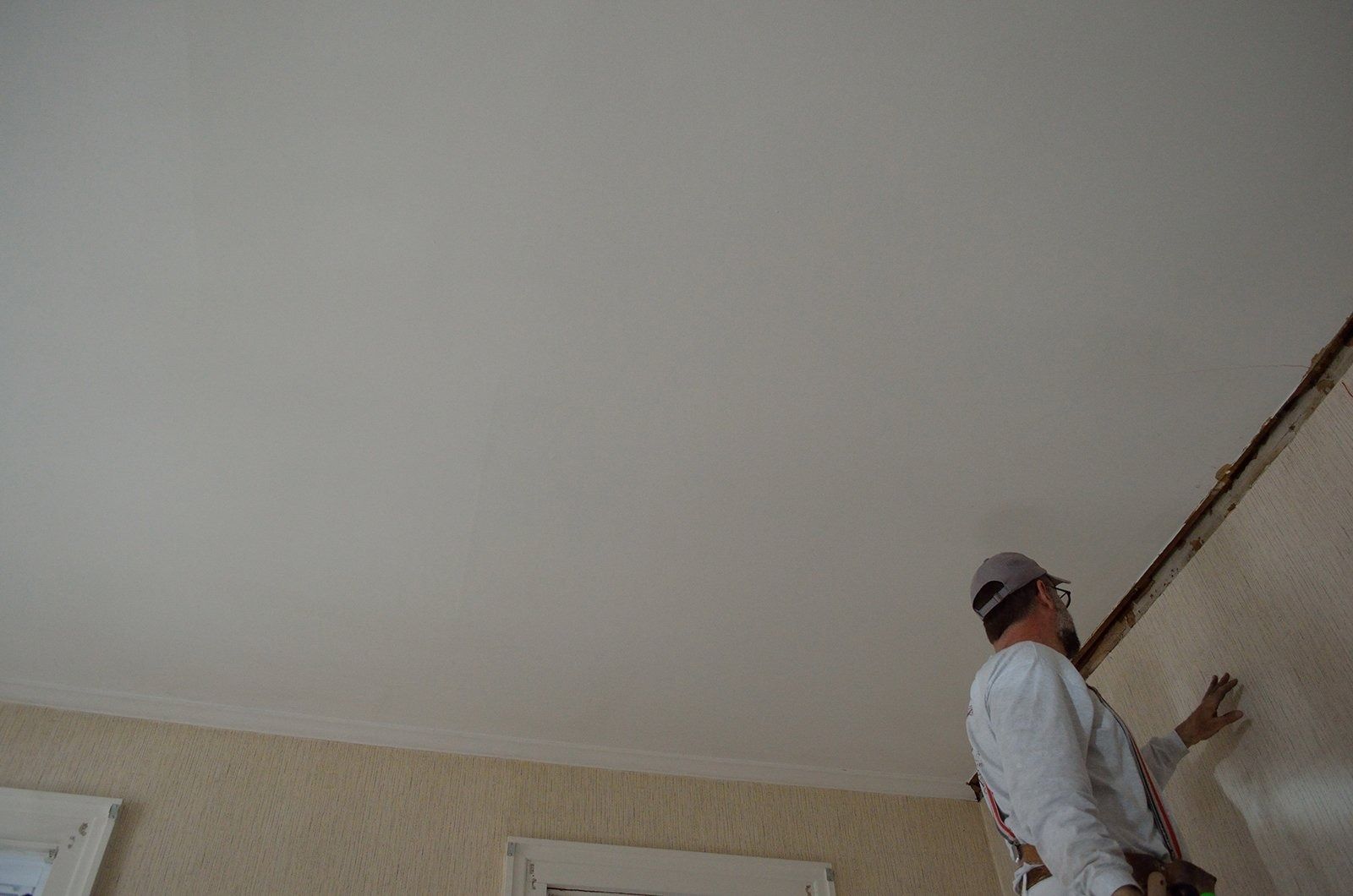Person painting a white ceiling and wall.