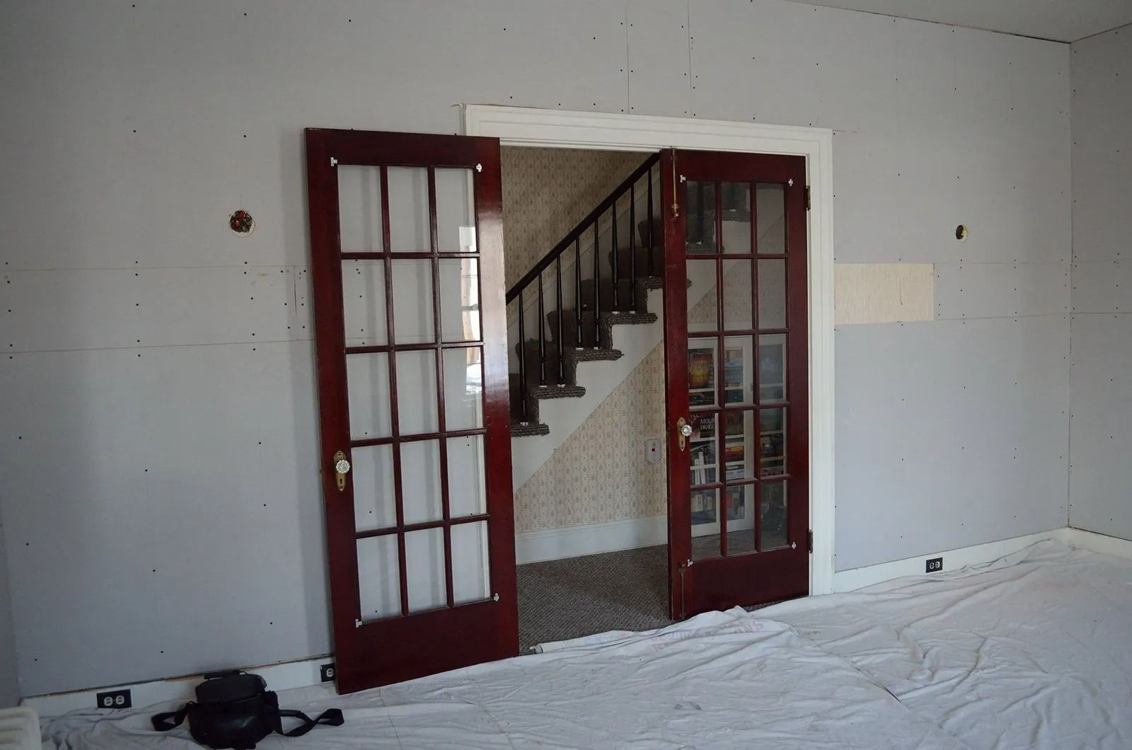 Pair of burgundy French doors open to a staircase. The walls are gray and there's a white tarp on the floor.