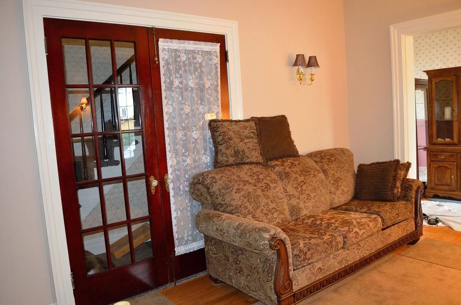 Brown sofa next to glass doors with sheer curtain; beige walls and light fixture.
