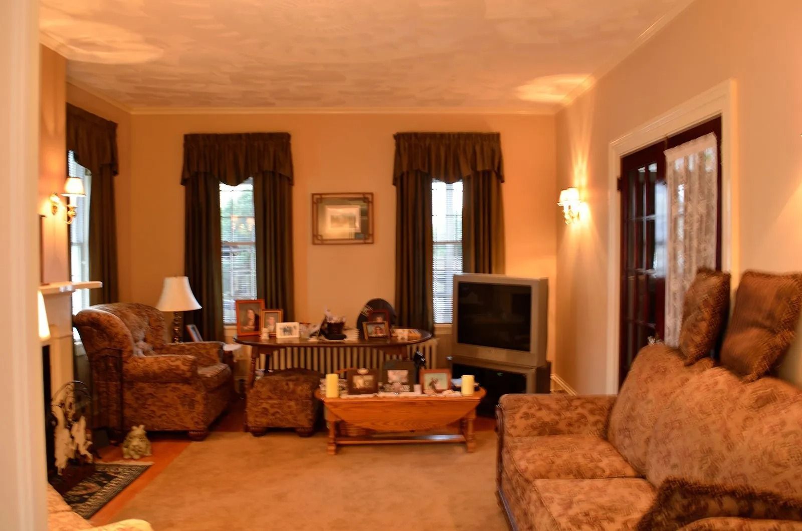 Living room with brown floral patterned furniture, beige walls, and dark brown curtains.