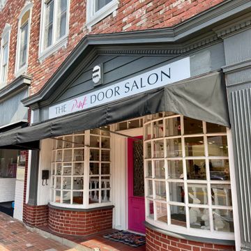 Storefront with gray awning and pink door for “The Pink Door Salon” on a brick building