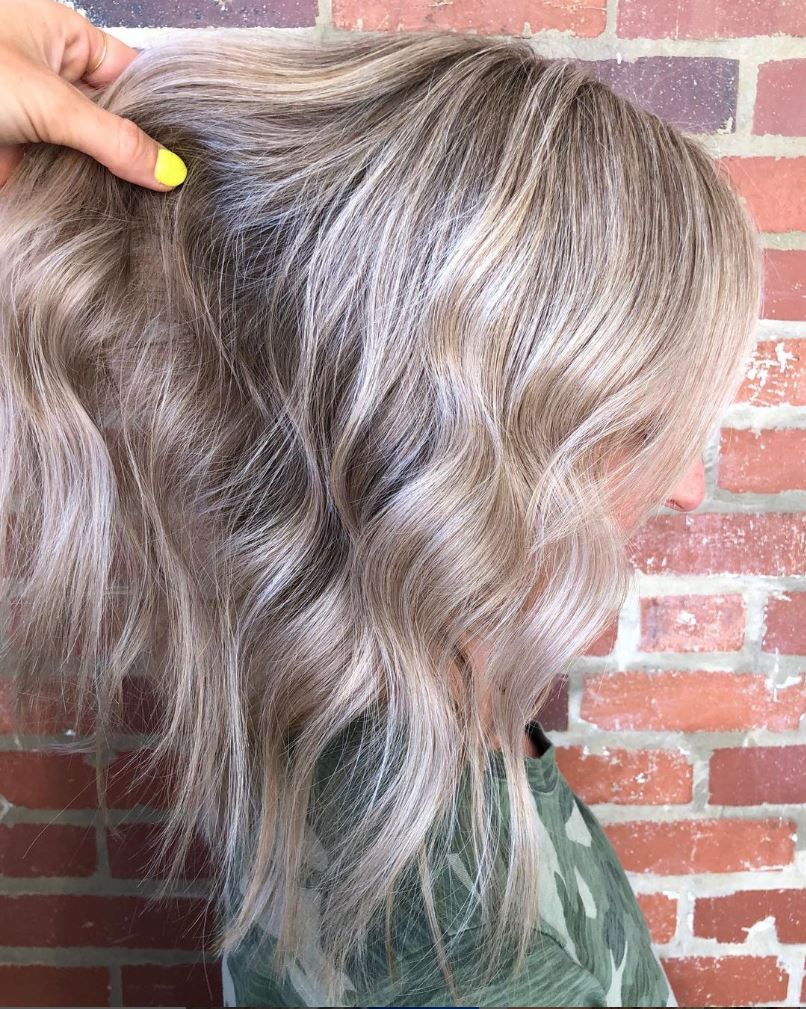 A woman with blonde hair is standing in front of a brick wall