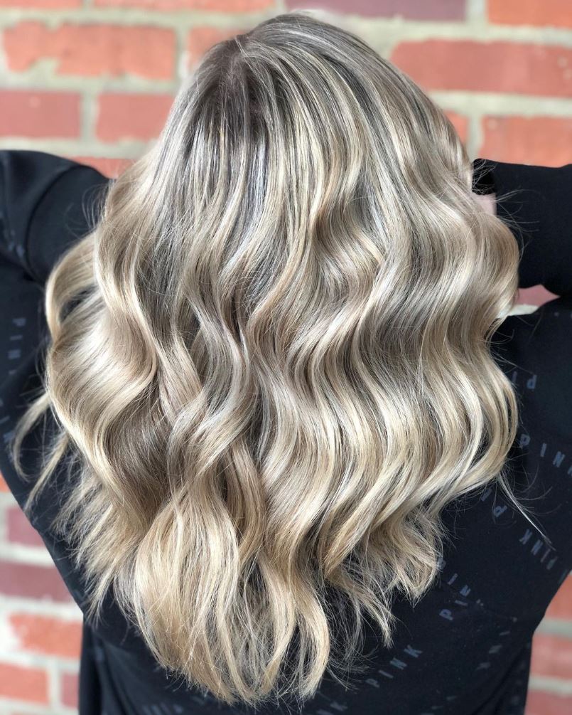 A woman with long blonde hair is standing in front of a brick wall