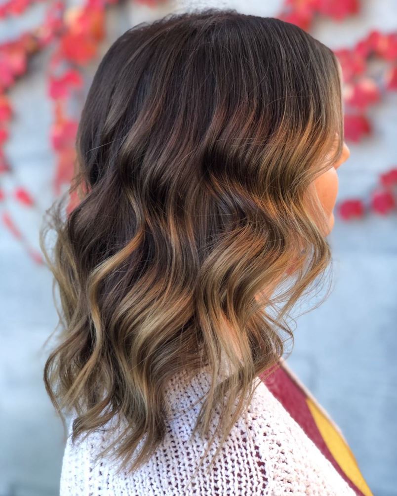 A woman with long wavy hair is wearing a white sweater and a scarf