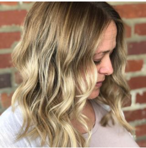 A woman with long blonde hair is standing in front of a brick wall