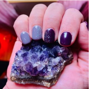 A woman with purple nails is holding a purple crystal in her hand.