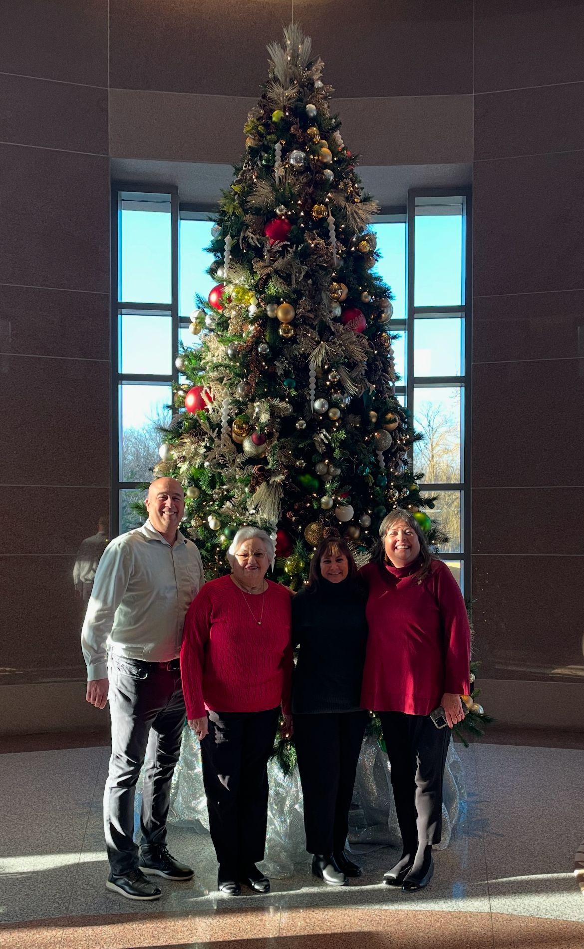 Four people pose in front of a decorated Christmas tree near a window.