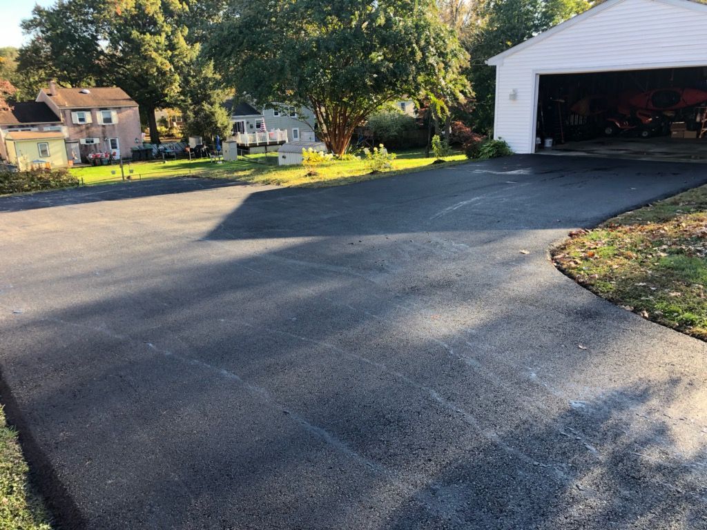 A driveway leading to a garage with a white house in the background