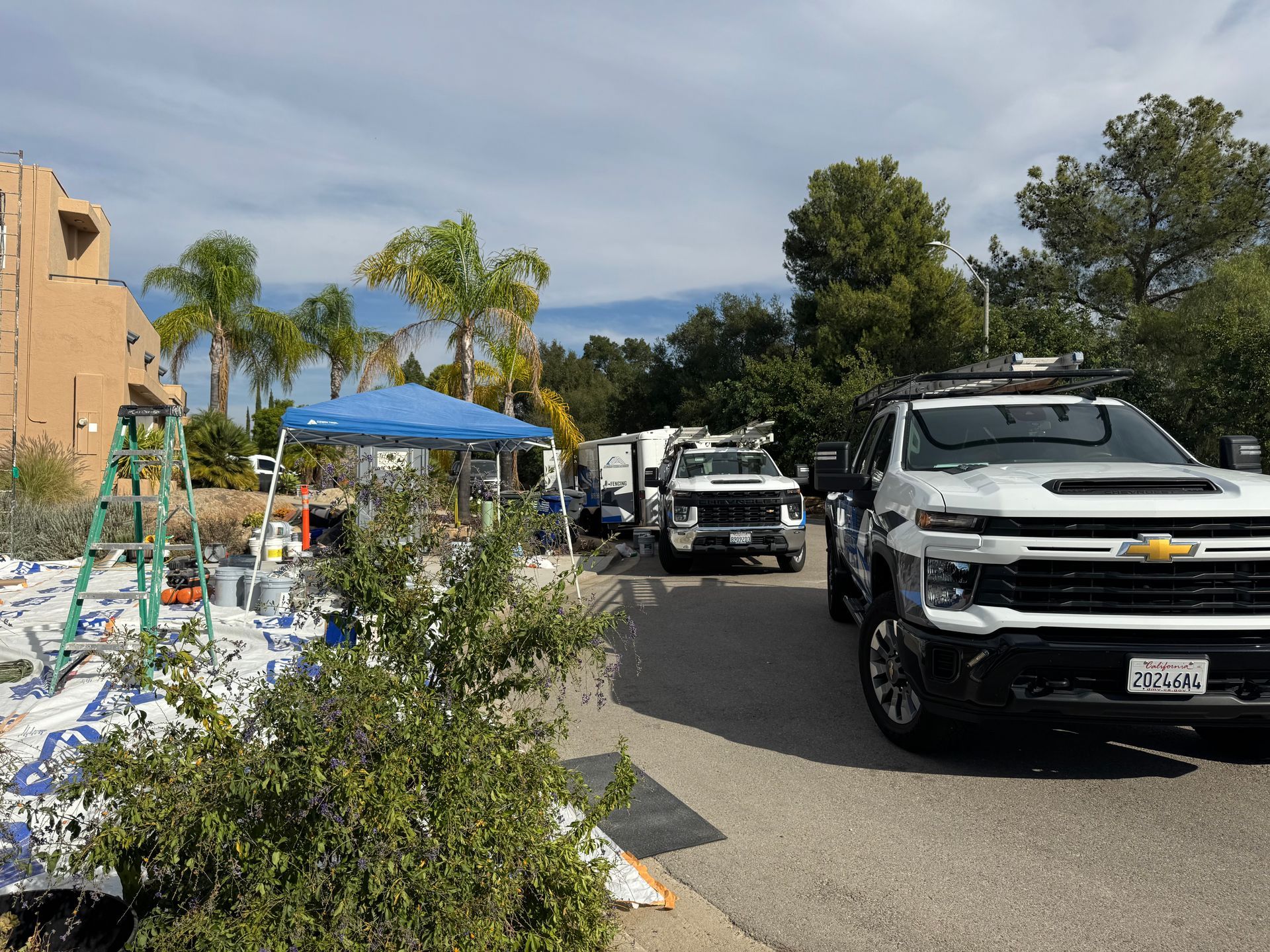 Construction site with trucks, a tent, and painting supplies. Building is visible in the background. Sunny day.