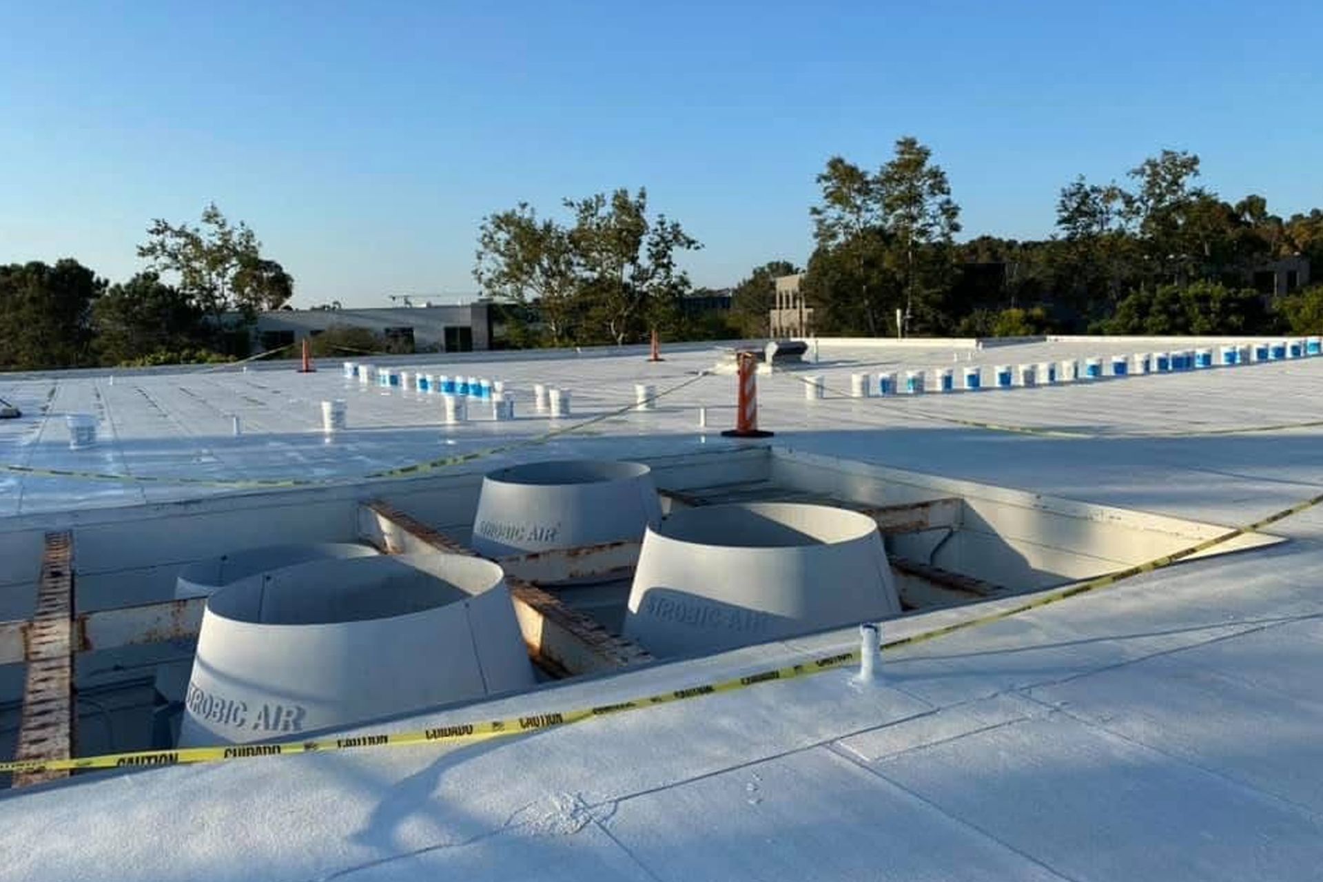 White flat roof with vents, buckets, and trees in the background. Construction in progress.