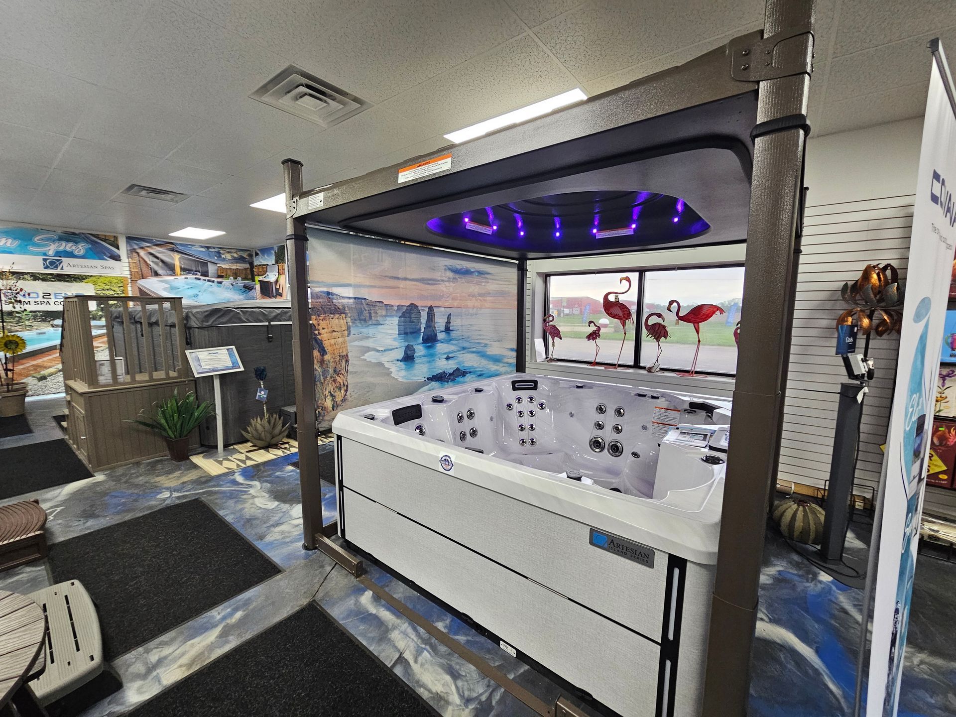 Indoor showroom with a white hot tub display lit by purple lights and ocean-themed wall murals