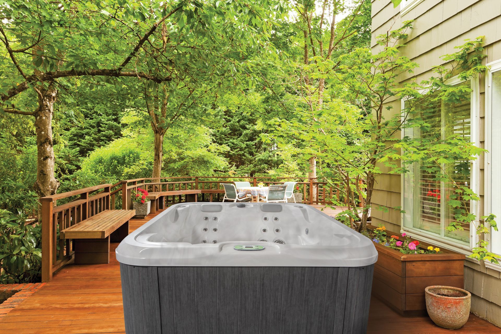Outdoor wooden deck with a large gray hot tub, surrounded by trees and a house