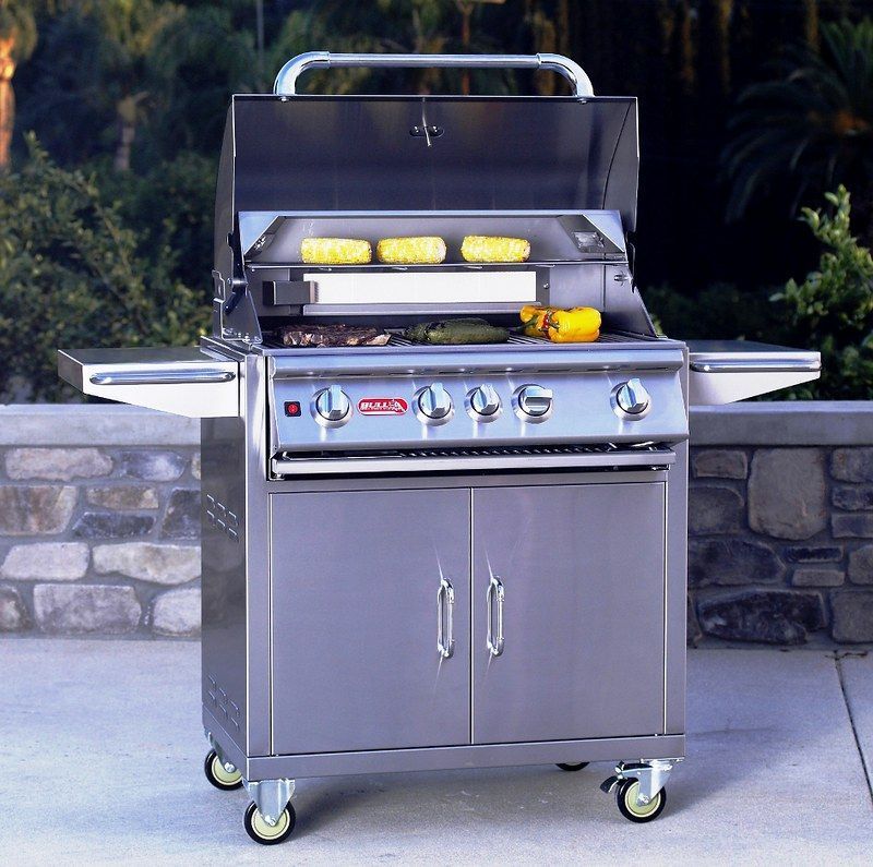 Stainless steel gas grill on a patio with the lid open, corn cooking on the grates, and side shelves extended