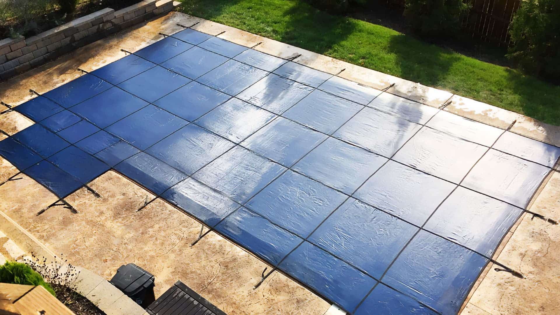 Blue-tiled patio or pool cover with a bright reflection, bordered by grass and stone paving.