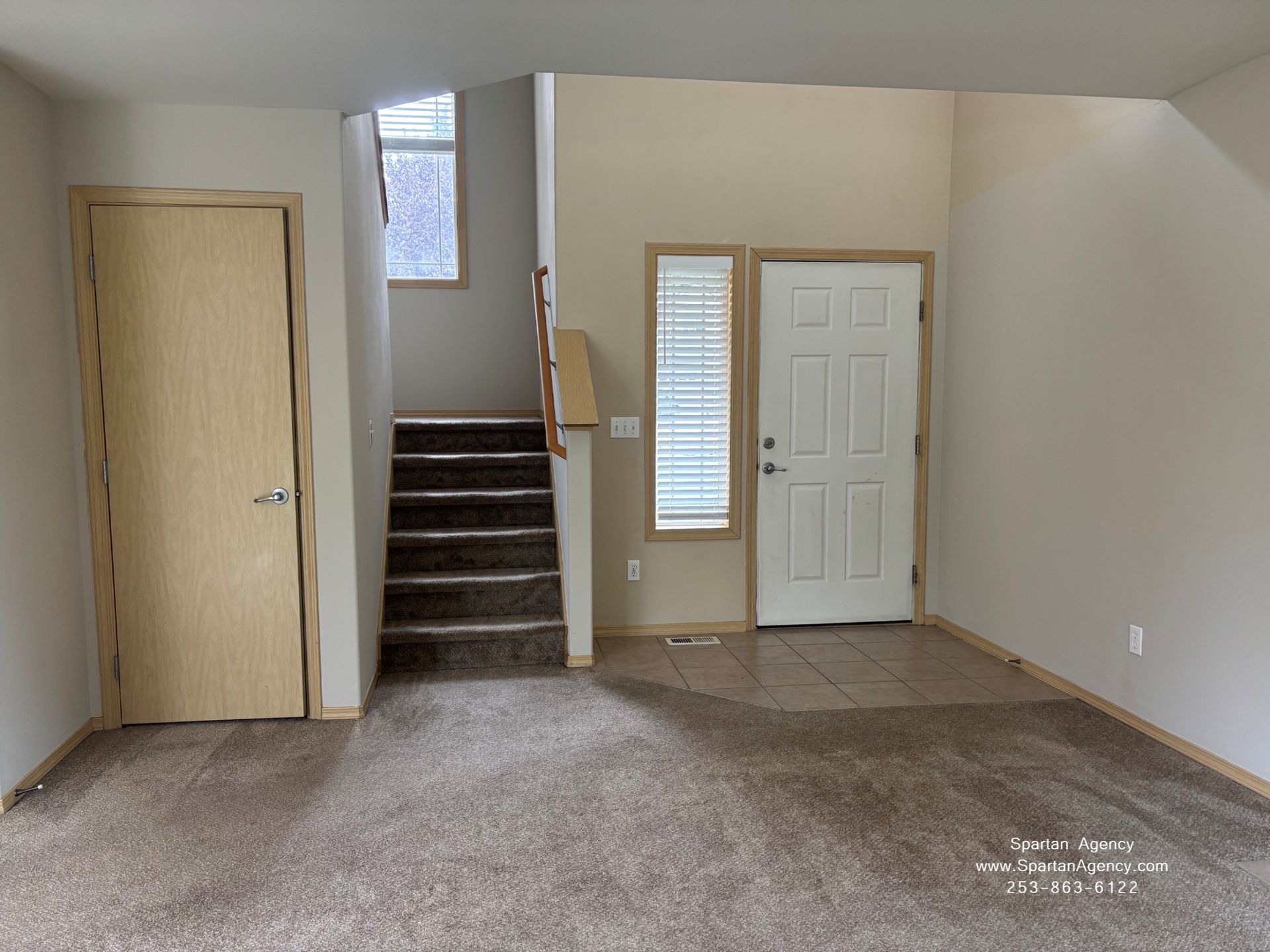 Empty carpeted room with stairs, a left door, and a front door with window sidelights.