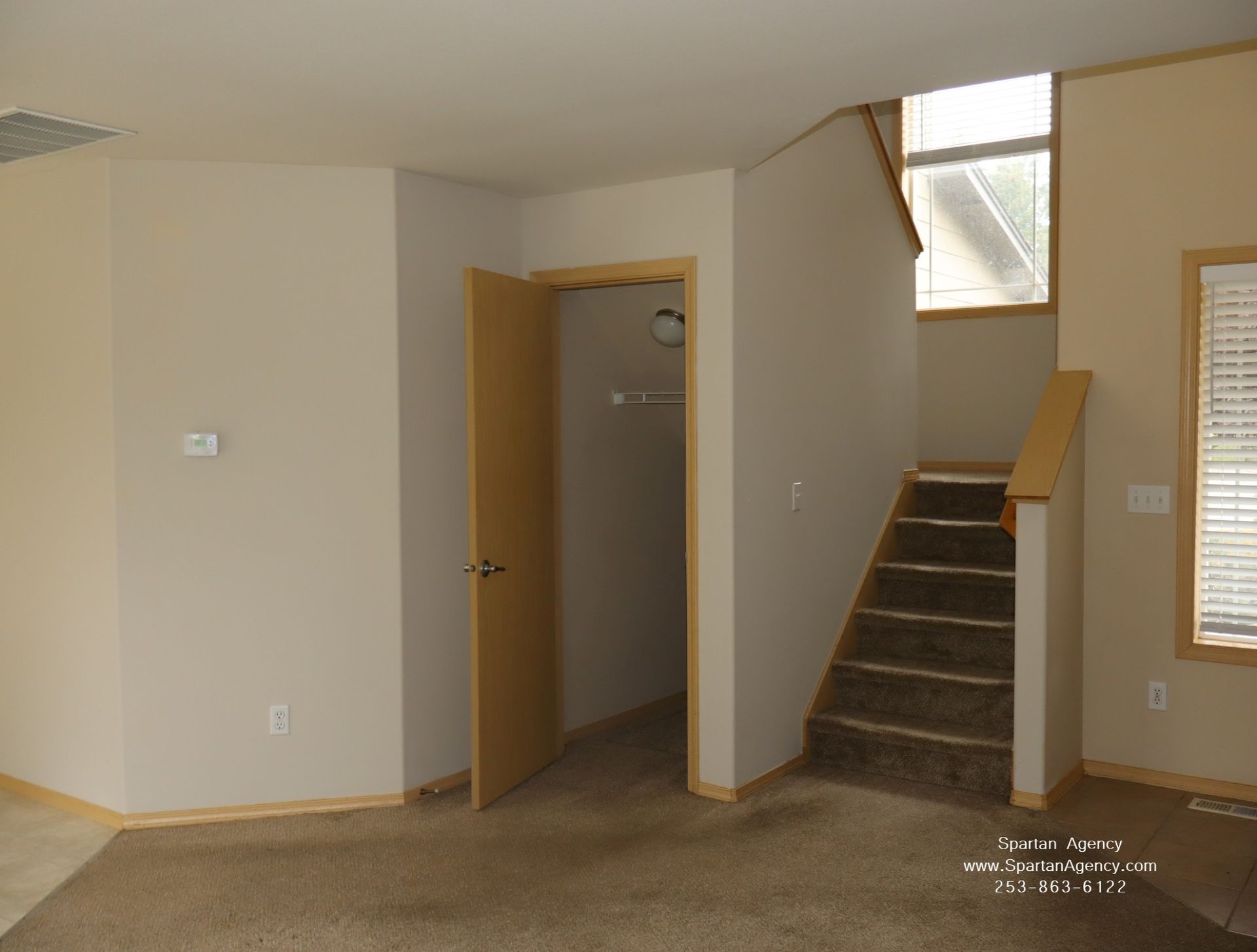 Empty room with beige walls, open door, and carpeted staircase under a small window.
