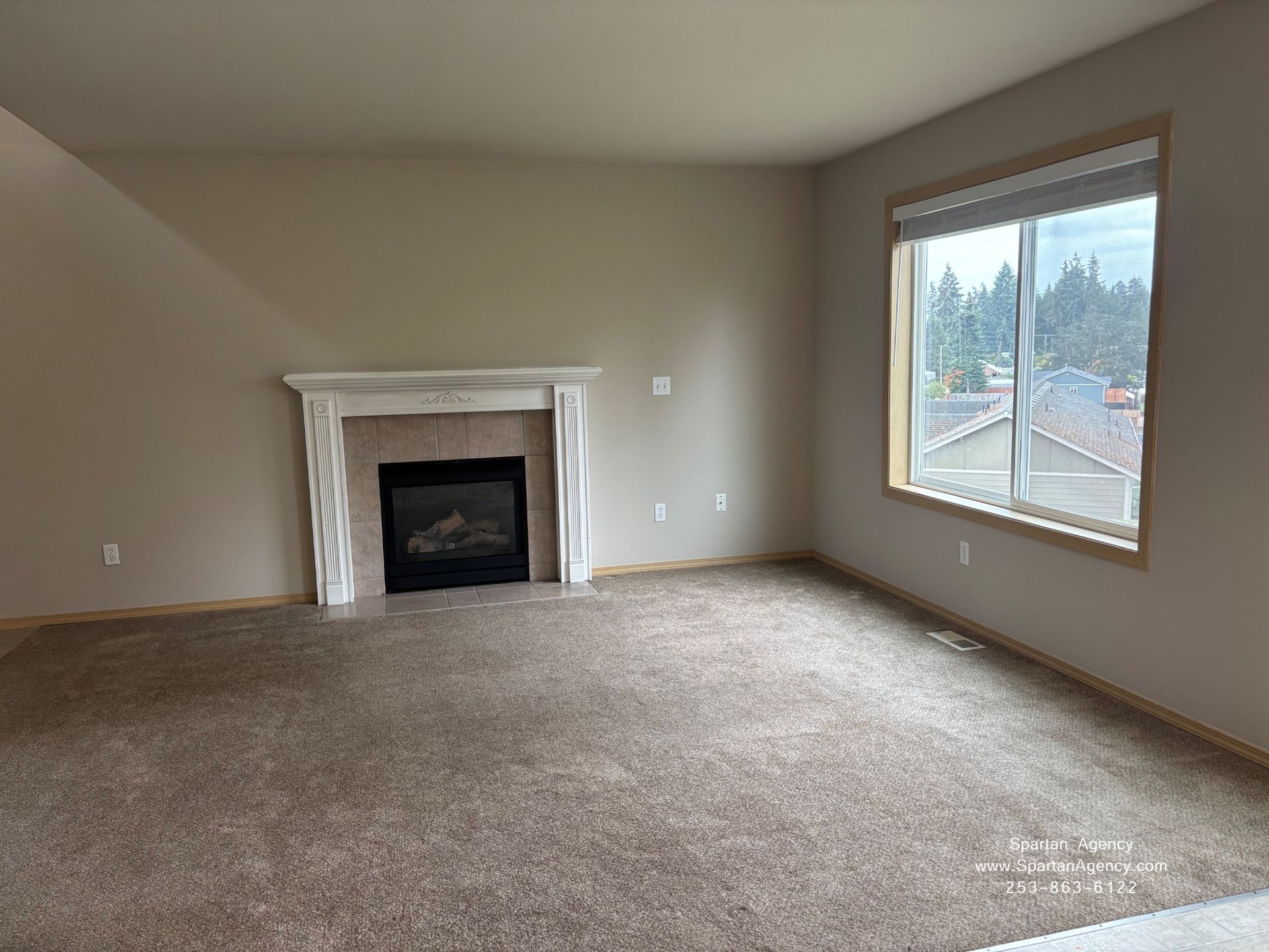Empty beige living room with carpet, fireplace, and large window