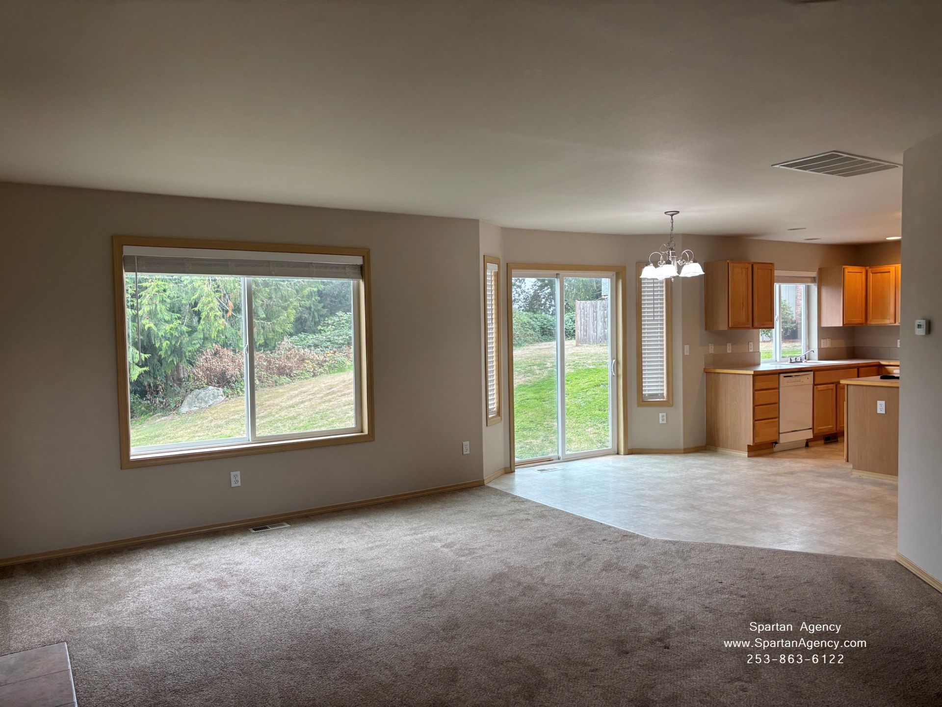 Empty living room and kitchen with carpet, tile floor, large windows, and backyard view