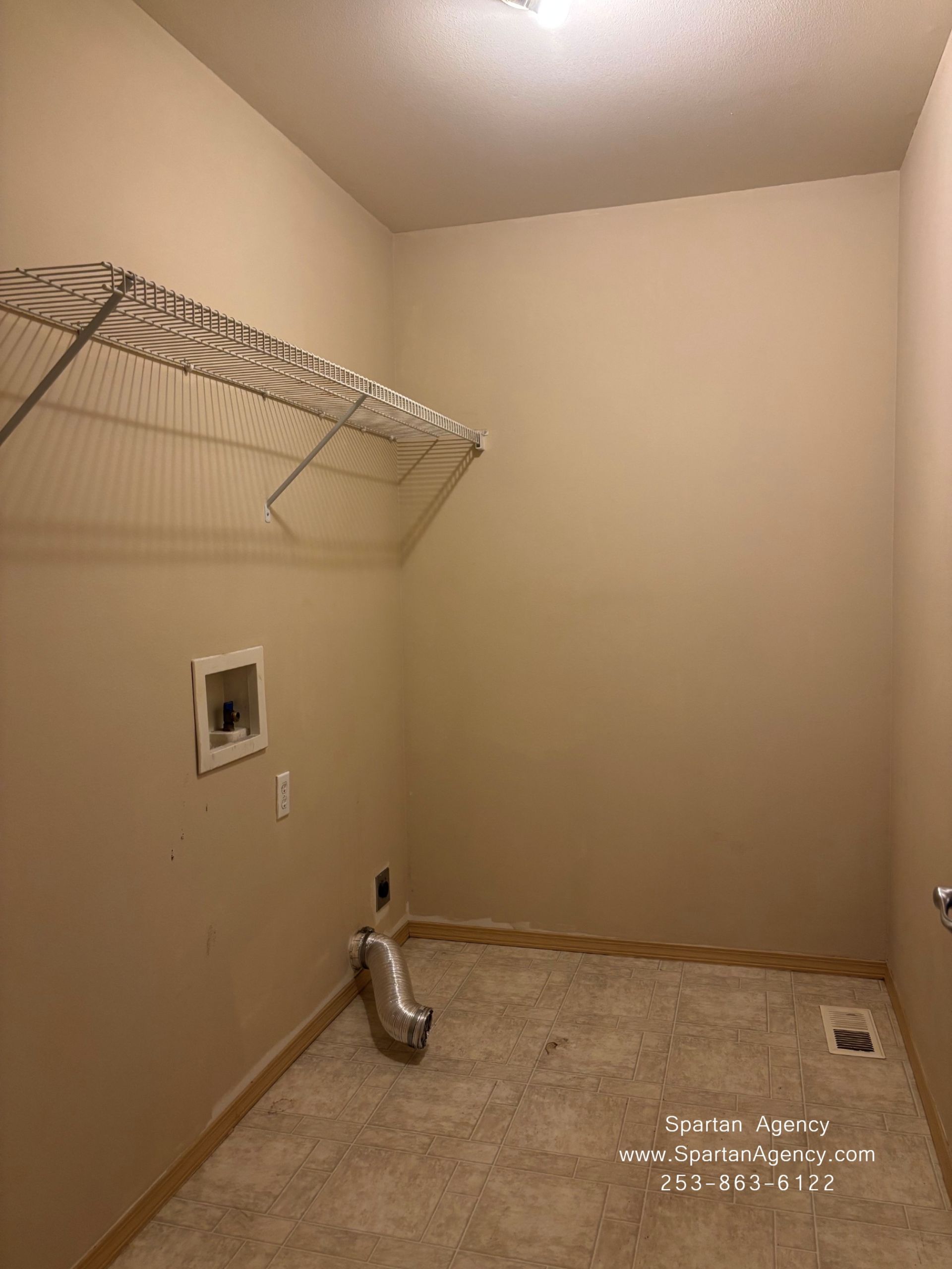 Empty laundry room with wire shelf, washer/dryer hookup, beige walls, and utility floor drain.