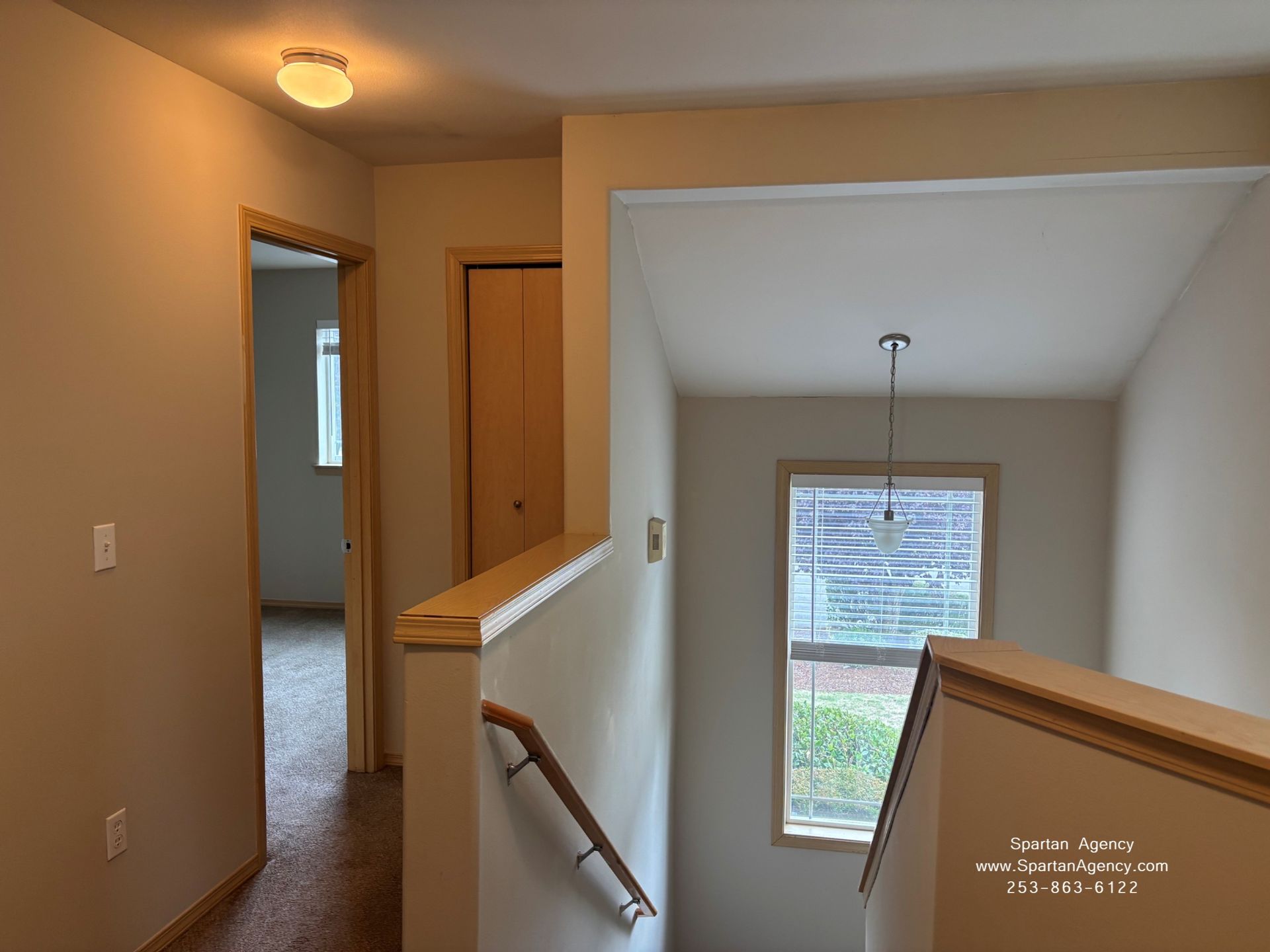 Stairway landing with beige walls, wooden railing, and a window at the end of the hall.