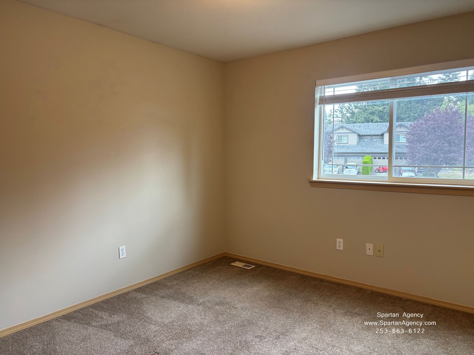 Empty beige bedroom with carpet and a window letting in daylight