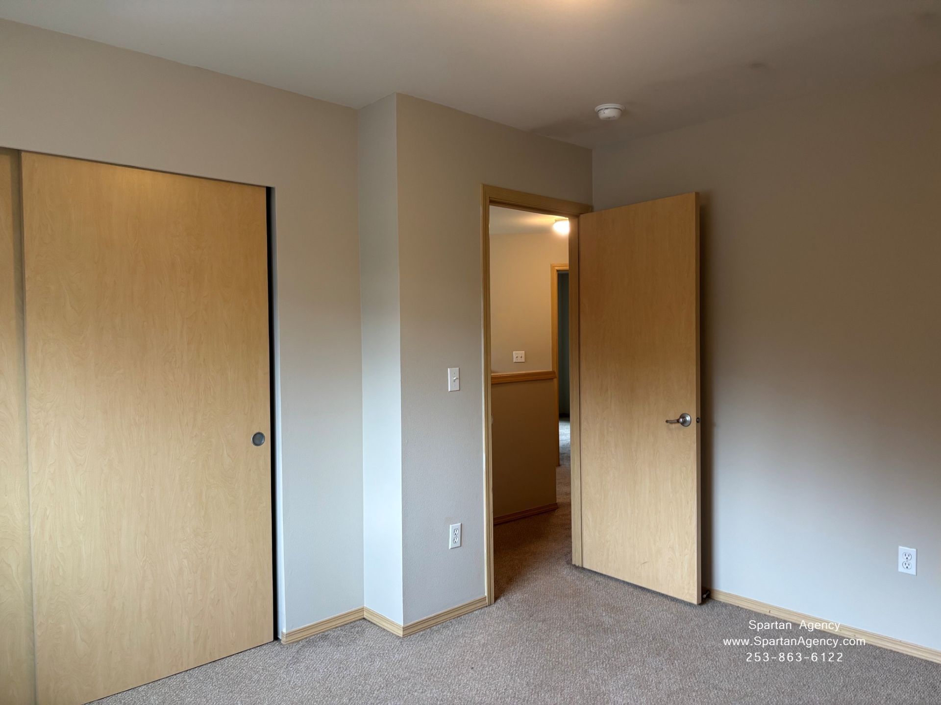 Empty bedroom with beige carpet, two closed closet doors, and an open doorway to a hall.