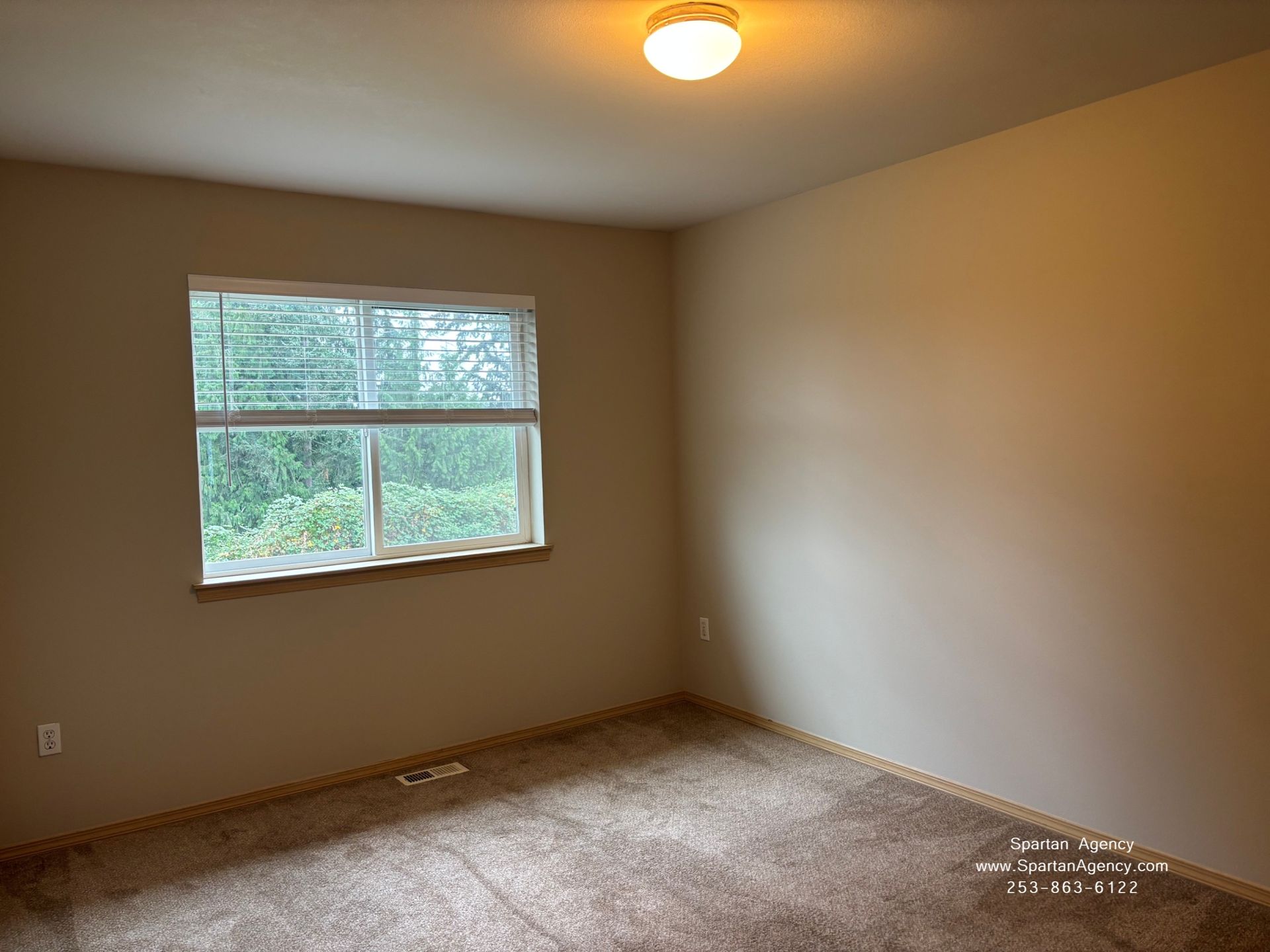 Empty beige bedroom with carpet, a window, and a ceiling light.