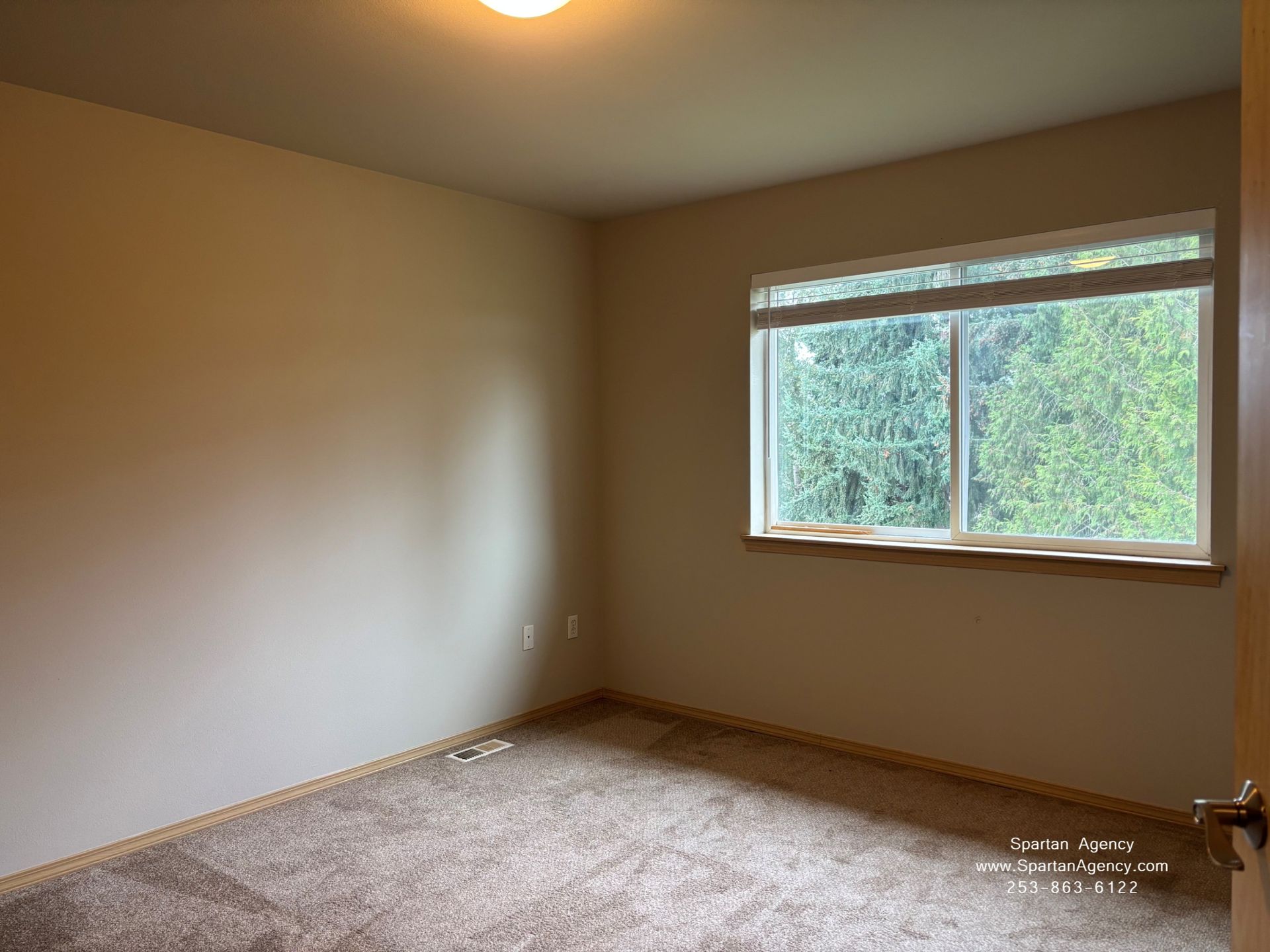 Empty beige bedroom with carpet, a window, and soft natural light.