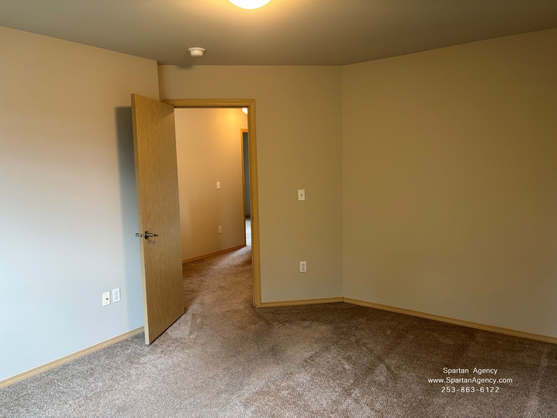 Empty beige bedroom with carpet and an open door leading to a hallway.