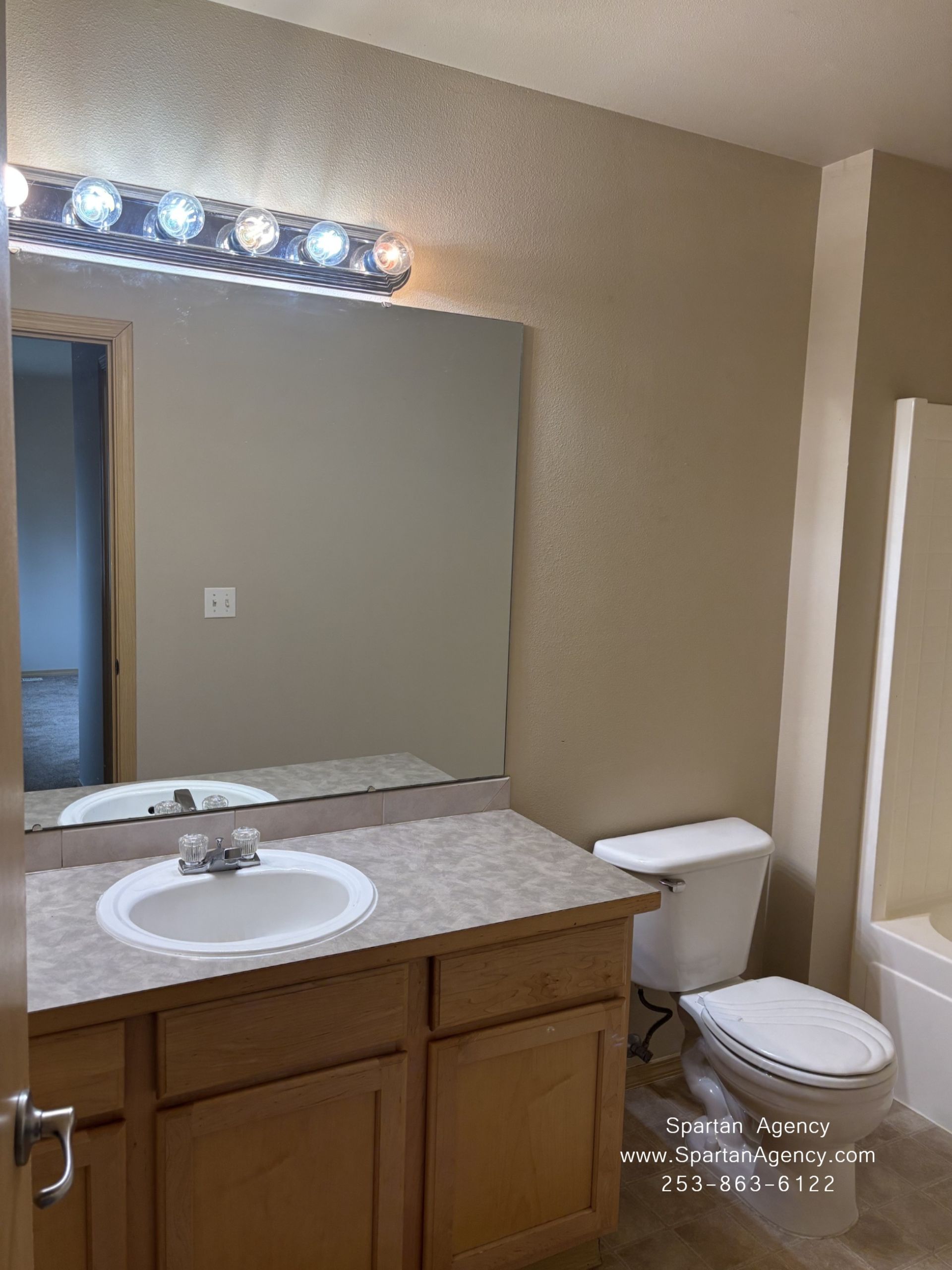 Bathroom with wood vanity, sink, large mirror, and toilet under a light fixture.