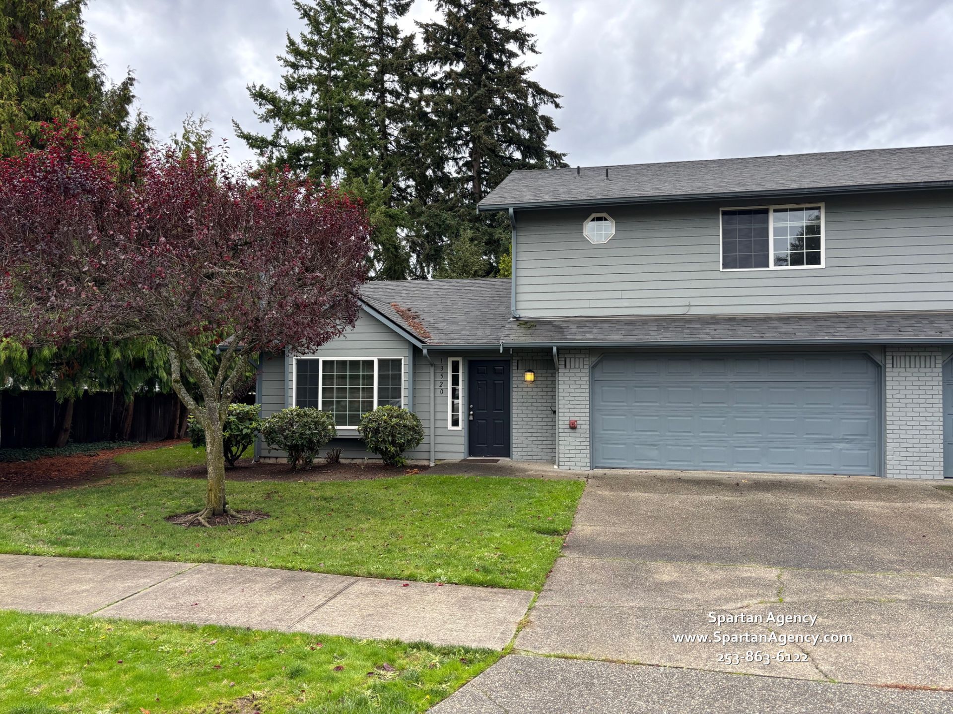 13520 107th Avenue Ct E, Puyallup, WA 98374 Two-story light blue house with a dark roof and front porch, surrounded by trees and a lawn.