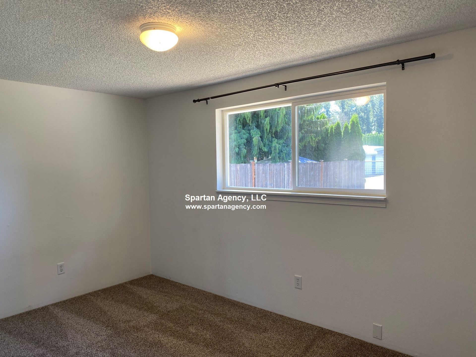 Empty bedroom with window and brown carpet. White walls and popcorn ceiling.