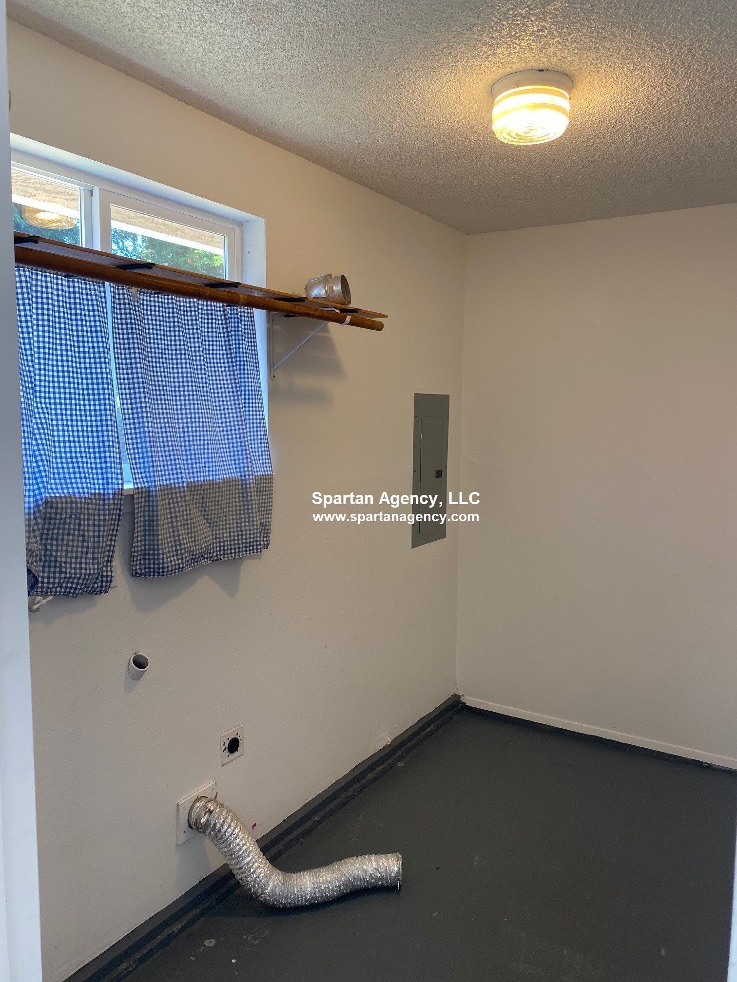 Laundry room with window and vent, dark floor and neutral walls.