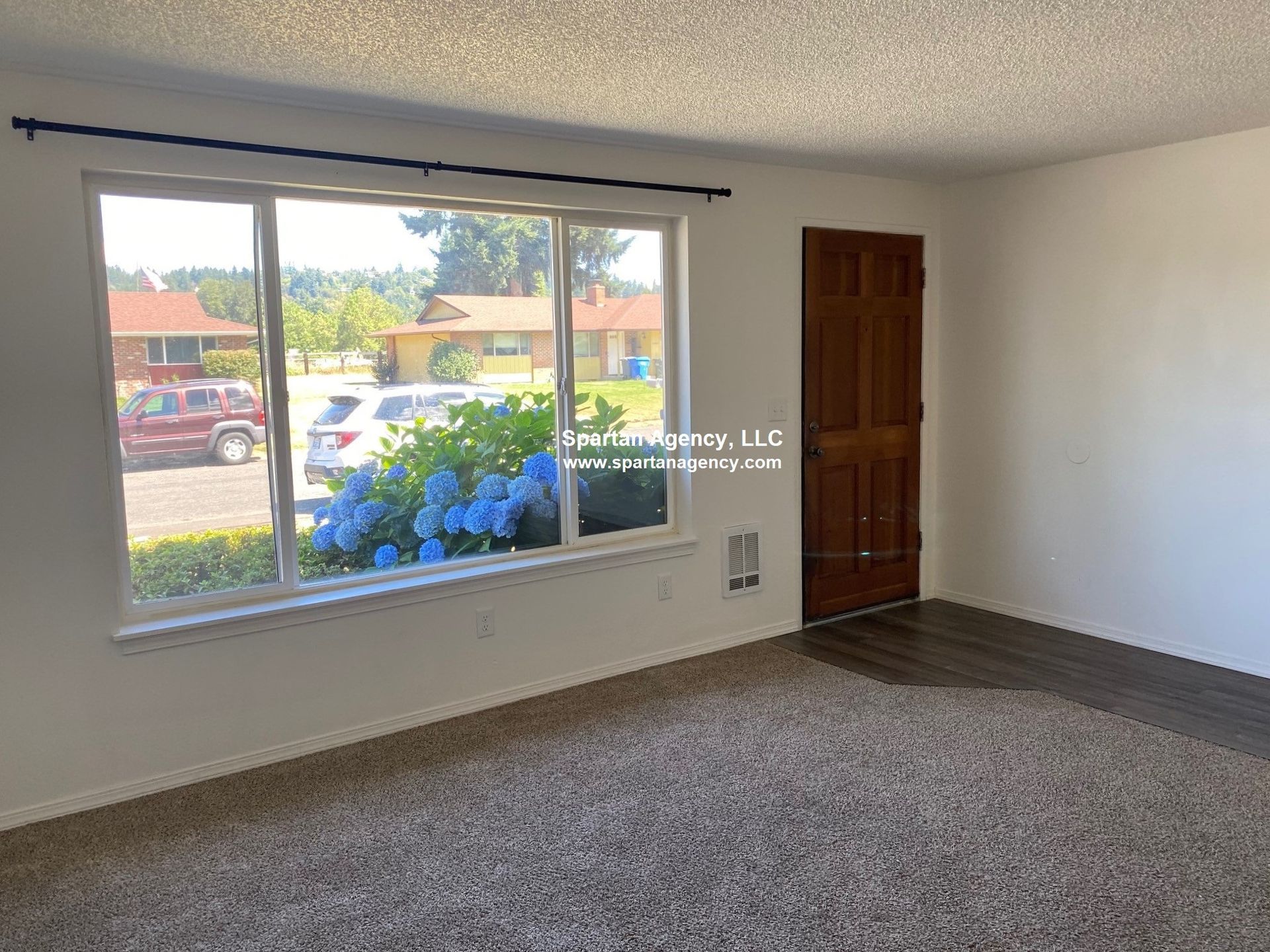 Interior of a room with a large window and brown door. Outside are houses and cars.