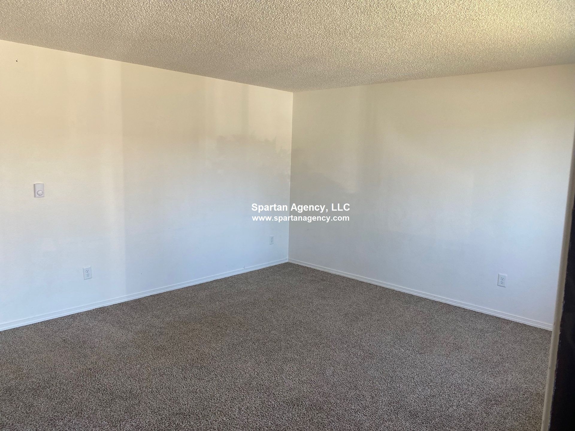Empty room with beige carpet, white walls and popcorn ceiling.