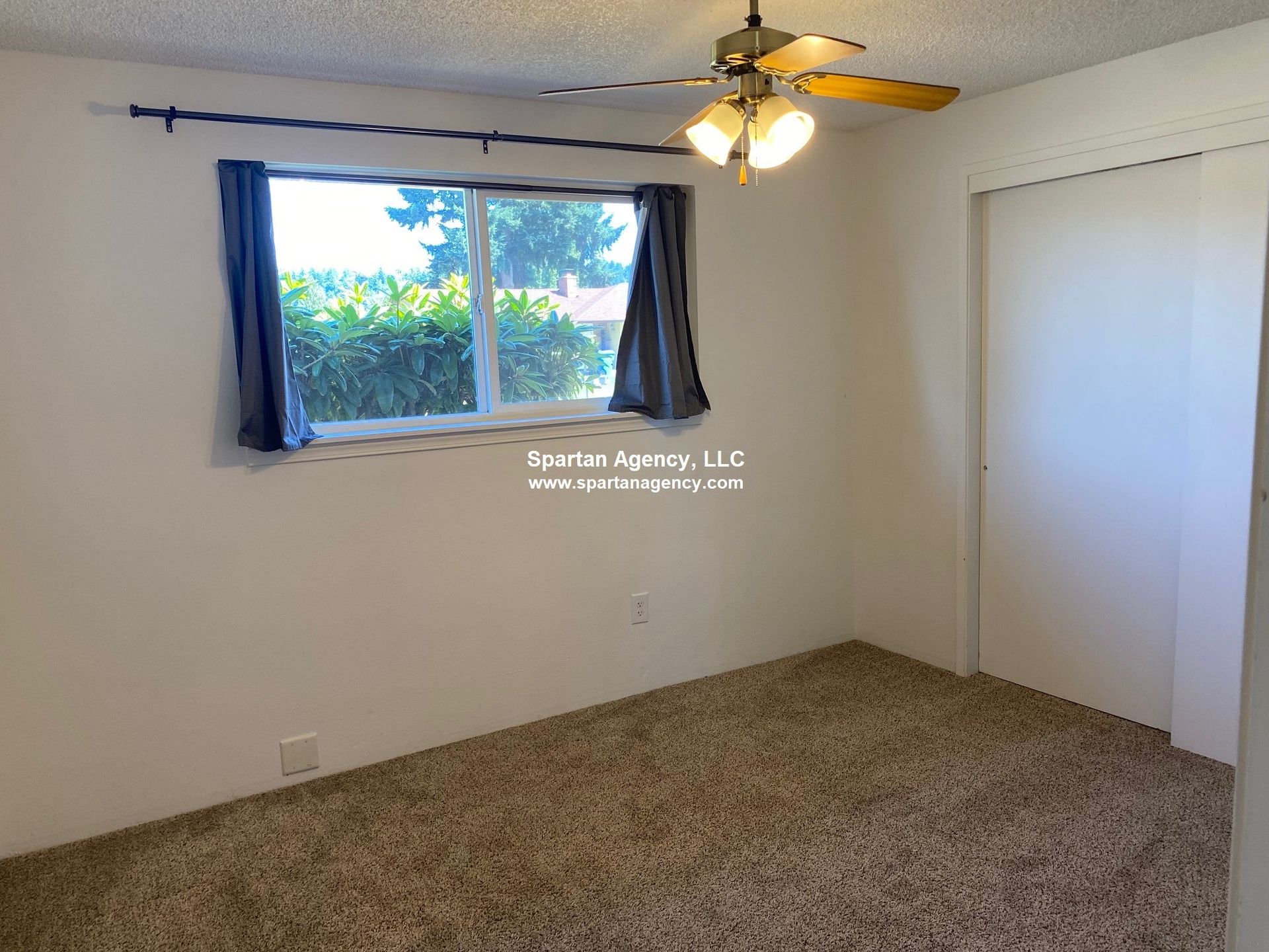 Bedroom with carpet, window with blue curtains, closet, ceiling fan.