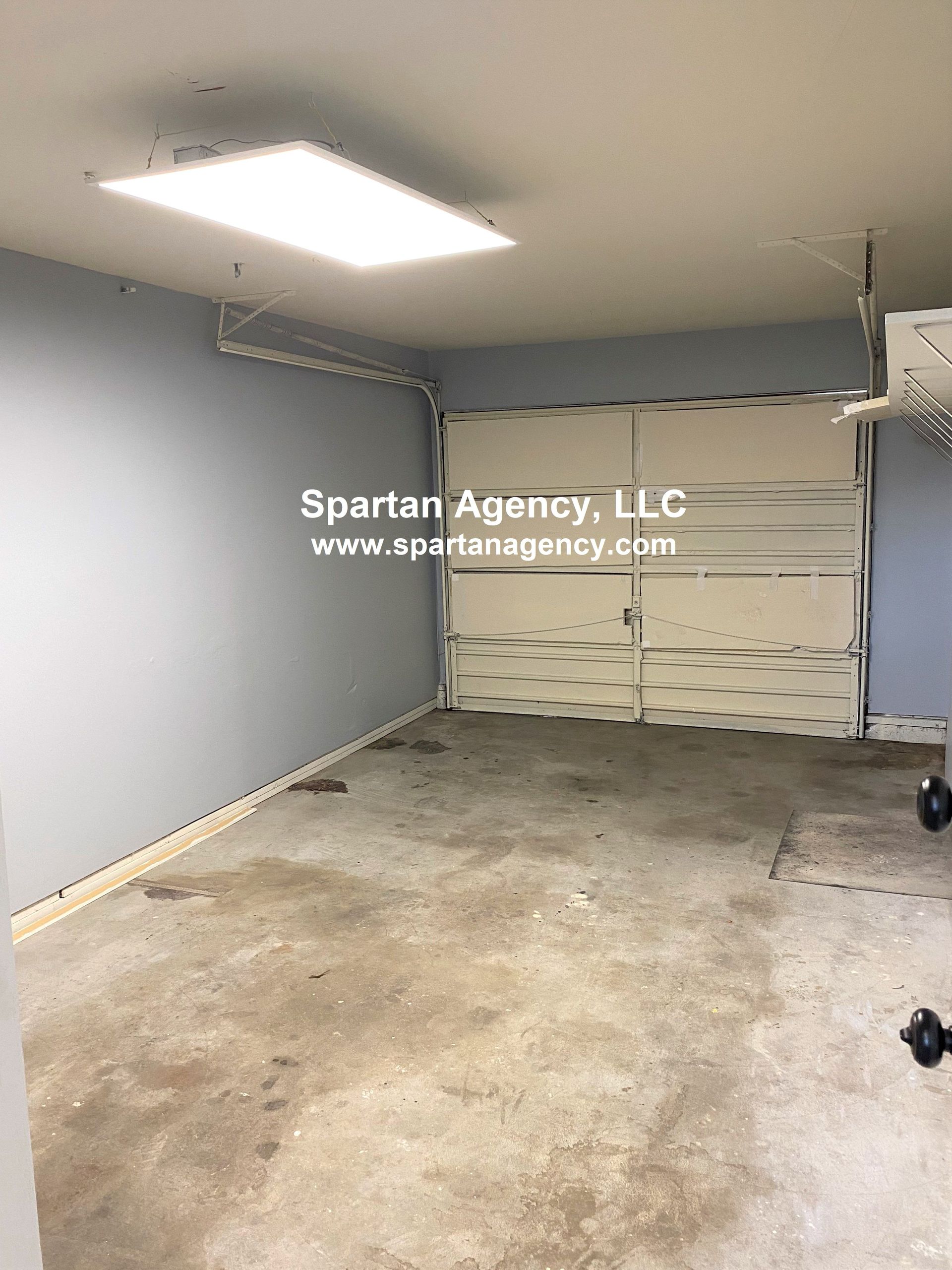 Empty garage interior with a closed white garage door, gray walls, and a dirty concrete floor.