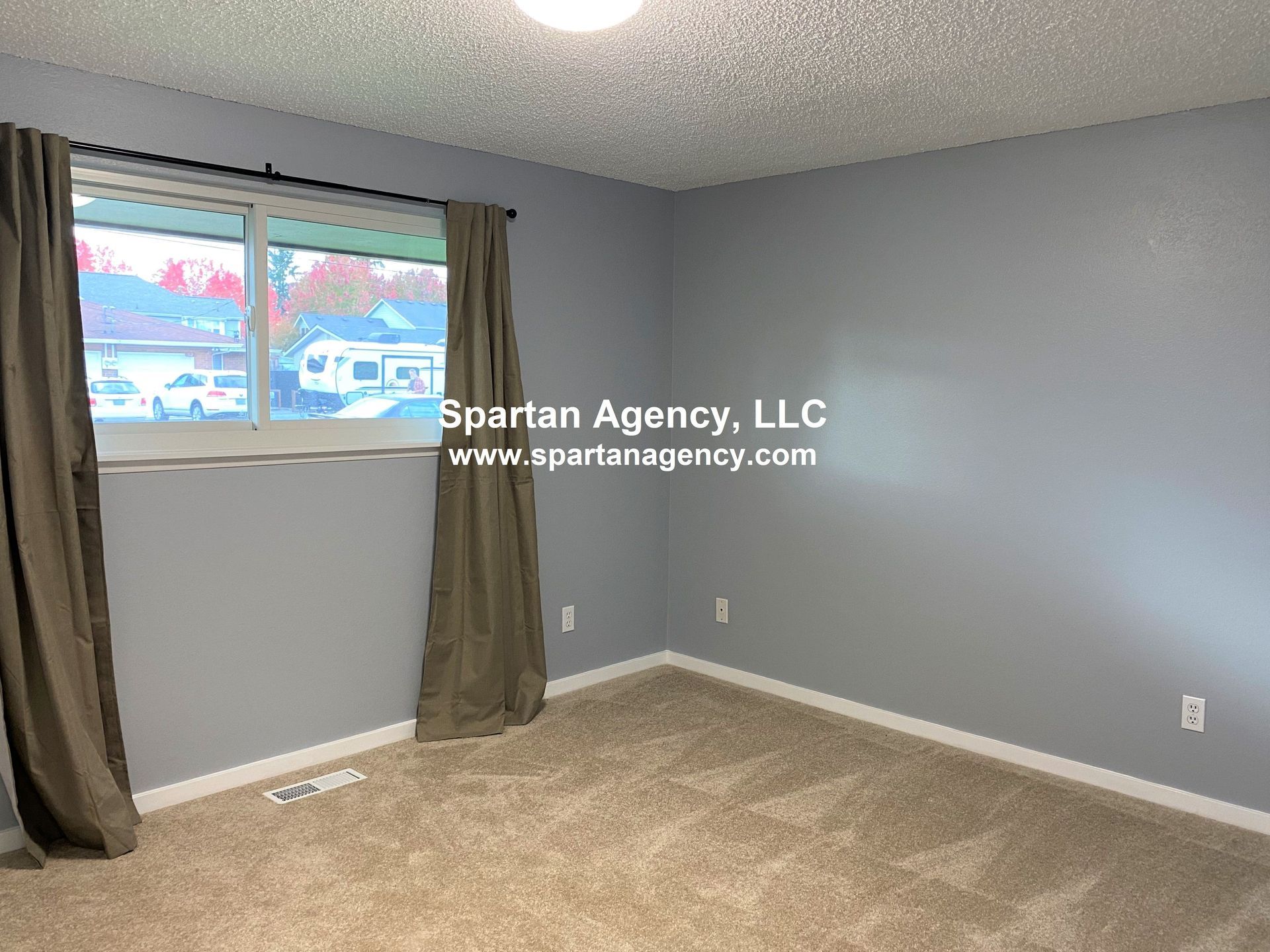 Empty bedroom with gray walls, brown carpet, a window, and brown curtains.